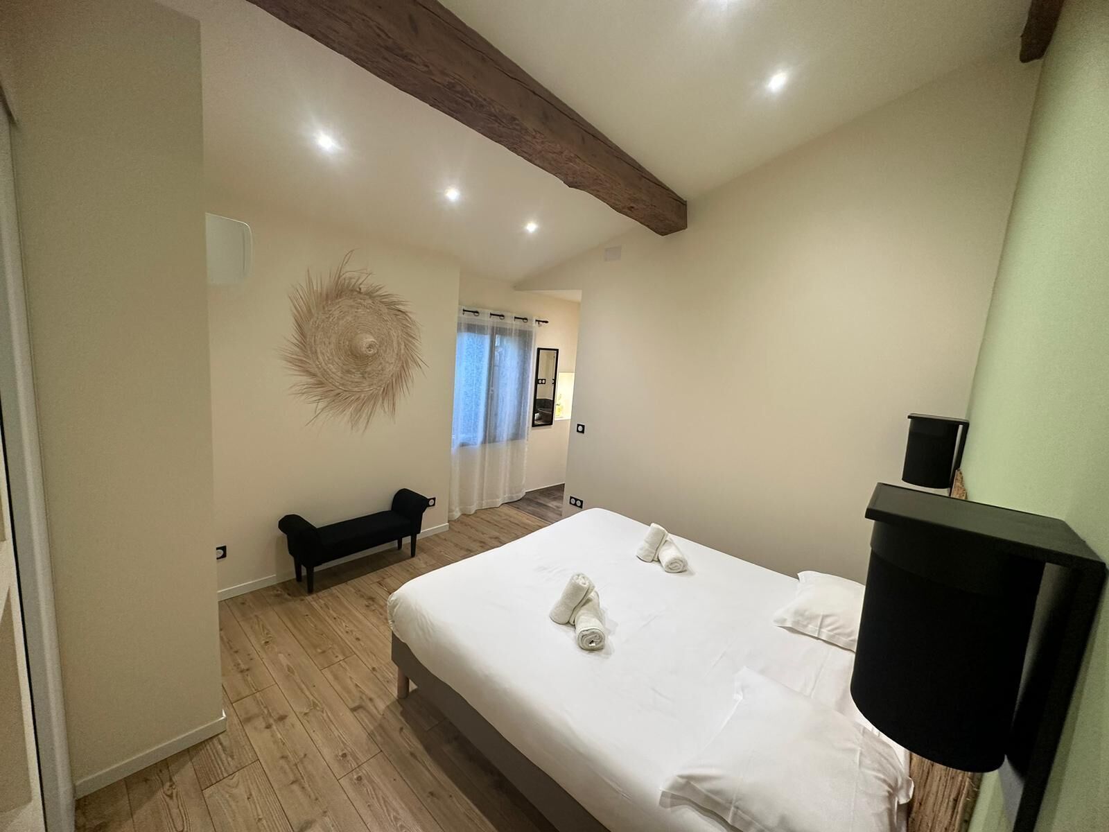 A bedroom with a large bed, a bench, a wall-mounted speaker, and a ceiling with exposed beams.