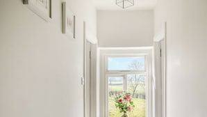 A hallway with a window at the end, a door, and a wall-mounted light fixture. - The Cottage at Brook Farm (Southwood, near Glastonbury)
