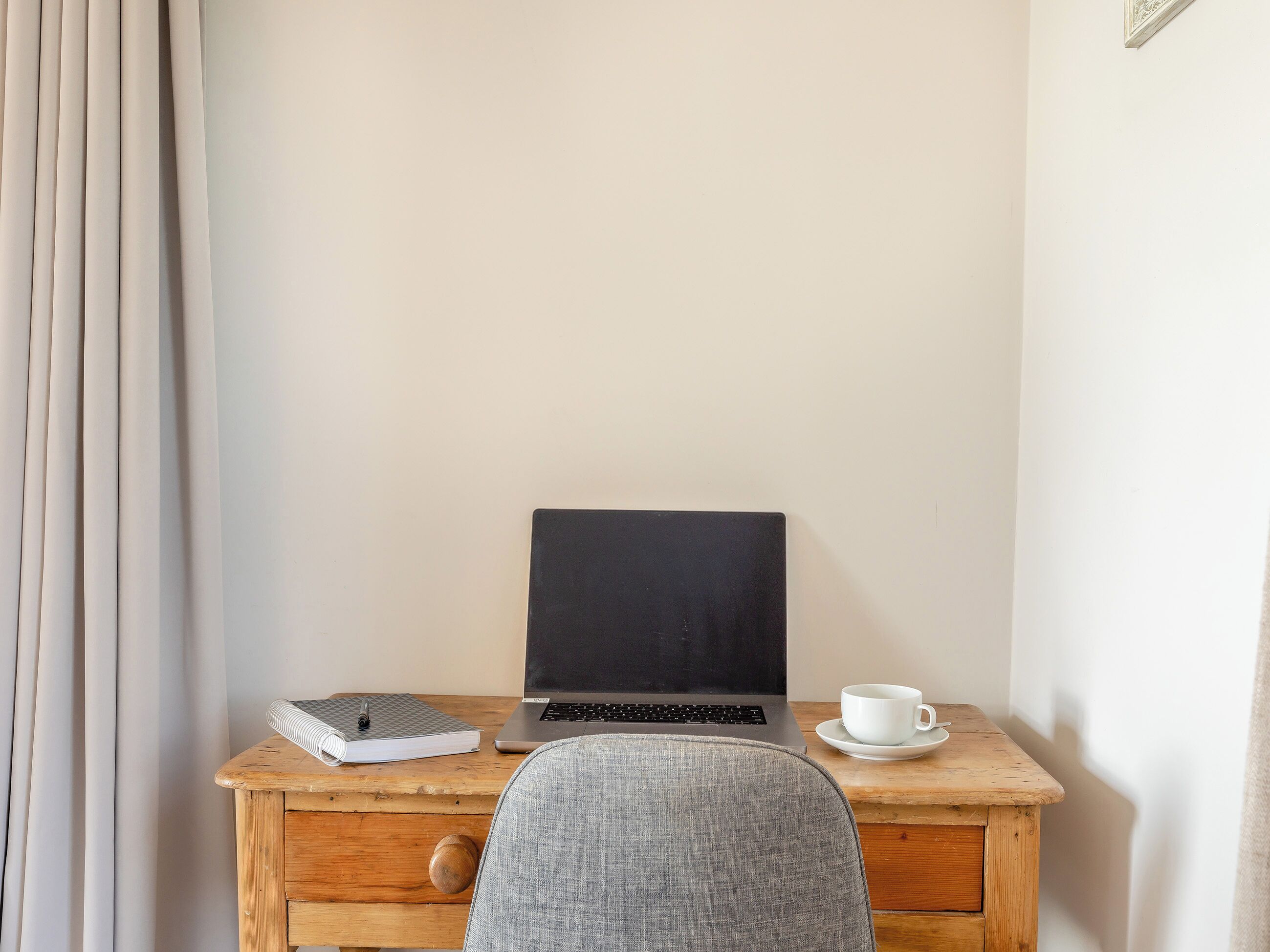 A wooden desk with a laptop, a notebook, and a cup.