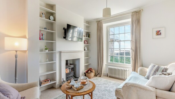 A living room with a fireplace, a television, and a large window with curtains. - The Cottage at Brook Farm (Southwood, near Glastonbury)