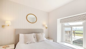 A bedroom with a bed, nightstands, a mirror, and a window with a view of the countryside. - The Cottage at Brook Farm (Southwood, near Glastonbury)