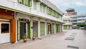 A street view of a building with green doors and windows, a shop on the ground floor, and a paved walkway. - Nivas Wanit (Bangkok)