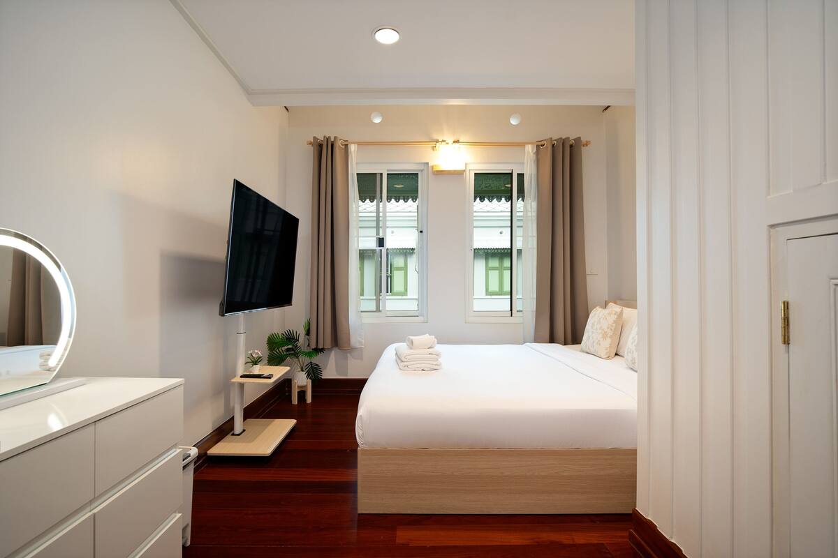 A hotel room with a bed, a TV, a desk with a computer, and a window with curtains.