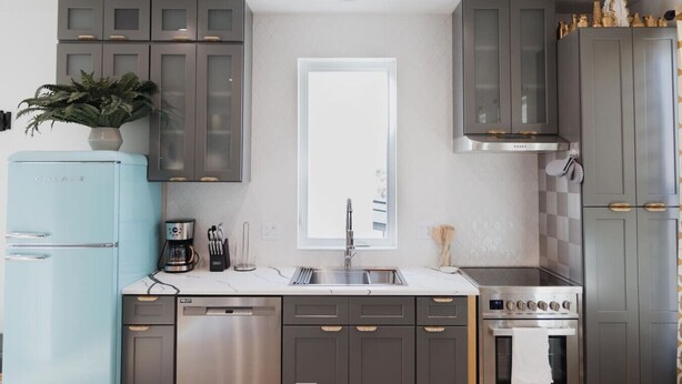 Une cuisine moderne avec des meubles gris, un réfrigérateur bleu, un évier en acier inoxydable et un four encastré.
