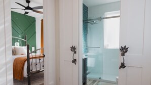 Une chambre d’hôtel avec un lit, un mur d’accent de couleur verte, un espace douche et une porte dotée d’une poignée décorative.