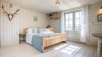 A room with a bed, a wooden ceiling, a chandelier, a window with curtains, and a door.