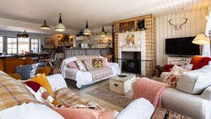 A cozy living room with a fireplace, a television, and a dining area with wooden furniture. - Camber Beach House - Five Bedroom Villa, Sleeps 10 (Camber)