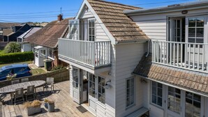 A two-story house with a balcony, a car parked in the driveway, and a wooden deck with outdoor furniture. - Camber Beach House - Five Bedroom Villa, Sleeps 10 (Camber)