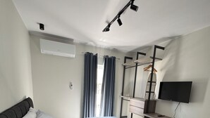 Un dormitorio moderno con cama, televisión, armario y lámpara en el techo.