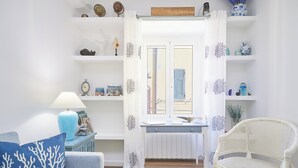 Ein Zimmer mit einem weißen Sessel, einem blauen Sofa, einem Tisch mit einer Lampe und Regalen mit Dekoration.