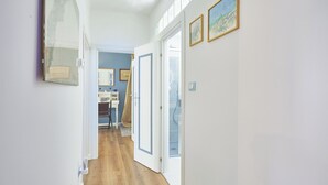 Ein Flur mit Holzboden, weißen Wänden und einer Tür zu einem Zimmer mit blauer Wand und Fenster.