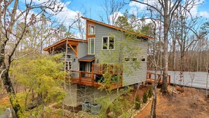 Eine zweigeschossige Holzhütte mit einer Holzterrasse, umgeben von Bäumen.