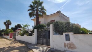 Una propiedad residencial con entrada portón cerrado, una palmera y un edificio blanco con puerta roja.