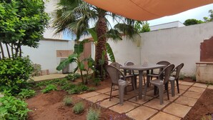 Un patio al aire libre con una mesa y sillas, rodeado de plantas y una palmera.