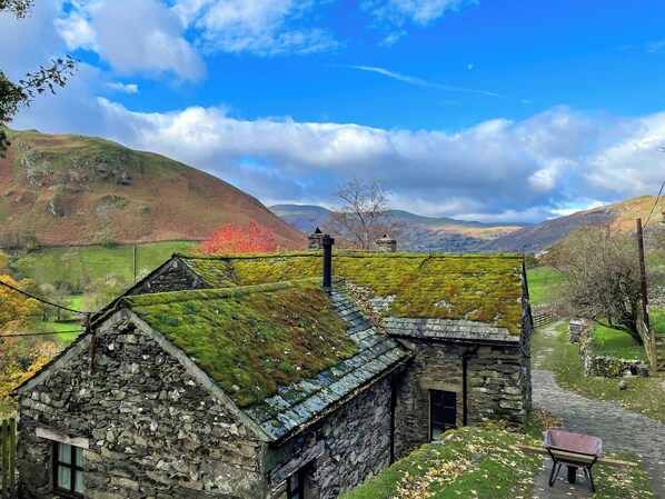 Ein Haus aus Stein mit einem moosbewachsenen Dach, einem Steinsschornstein und einem kleinen Fenster.