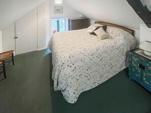 Ein Schlafzimmer mit einem Bett, einem Sessel, einer Kommode und einer Tür zu einem weiteren Raum.