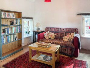 A cozy living room with a bookshelf, a red sofa, a patterned rug, and a small table with a magazine.