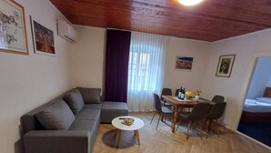 A living room with a sofa, a dining table with chairs, a small round table with a bowl, and a bed in the background. - Three-bedroom apartment with balcony (Dubrovnik)