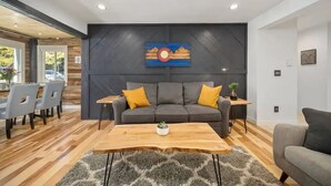 Un salon moderne avec un canapé gris, une table basse en bois et une grande œuvre d’art accrochée au mur.