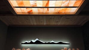A spa room with a wooden ceiling, a wall-mounted light display, and two massage tables.