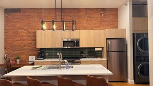 A modern kitchen with a brick wall, wooden cabinets, stainless steel appliances, and a central island with chairs.
