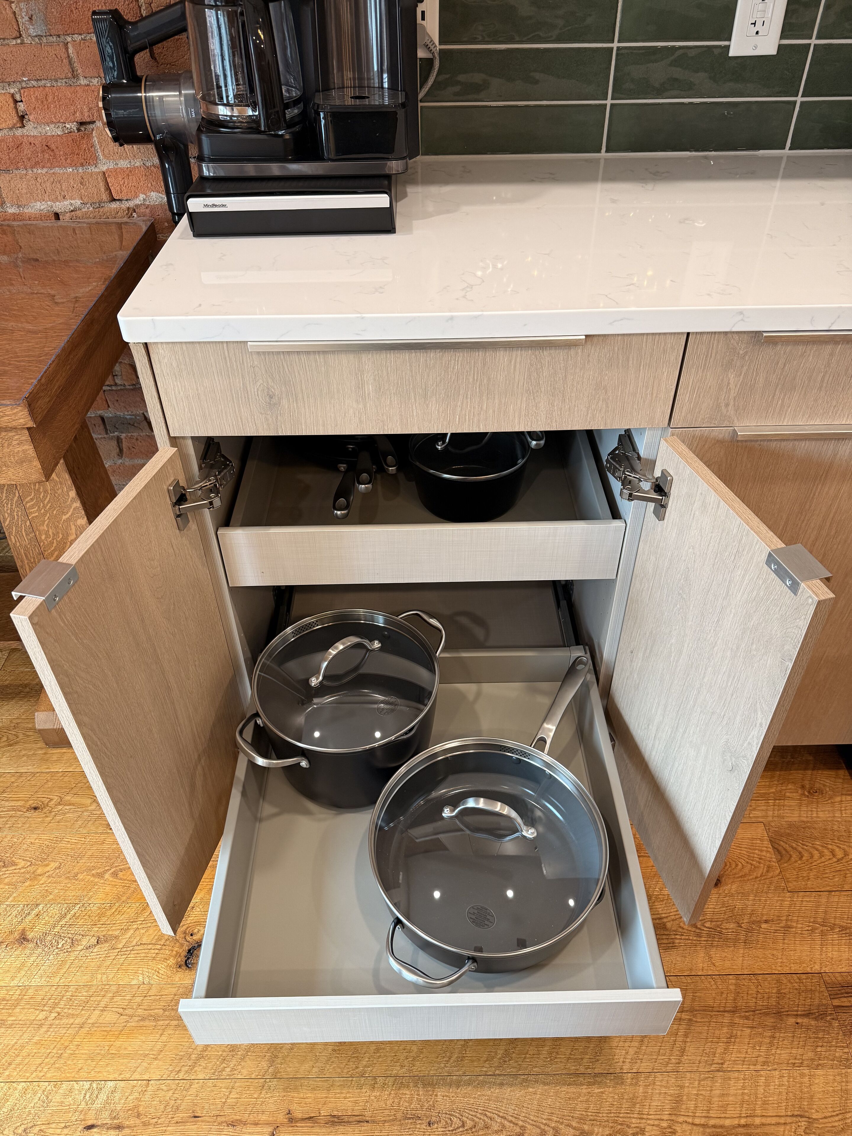 A kitchen with a coffee maker on the counter and two pots in a drawer.