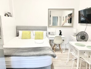 Een hotelkamer met een bed, een bureau, een stoel, een spiegel, een televisie en een ventilator.