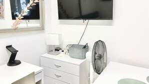 A modern room with a flat-screen TV mounted on the wall, a white dresser with drawers, a desk with a computer, a standing fan, and a decorative butterfly wall art piece. - Flat 2  (London)