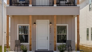 Une maison à deux étages avec un porche à l’avant, un balcon à l’étage supérieur et une porte d’entrée ornée d’une plaque numérotée.