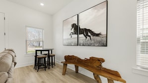 Un salon moderne avec un banc en bois, un coin repas avec des tabourets et une grande œuvre d’art sur le thème des chevaux accrochée au mur.