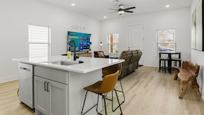 Une cuisine moderne avec un îlot central blanc, des tabourets de bar, une table à manger avec des chaises et un ventilateur de plafond.