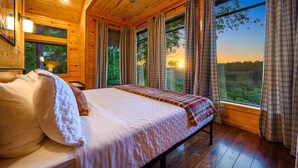 Ein Schlafzimmer einer Holzhütte mit einem Bett, Vorhängen und Blick ins Freie.