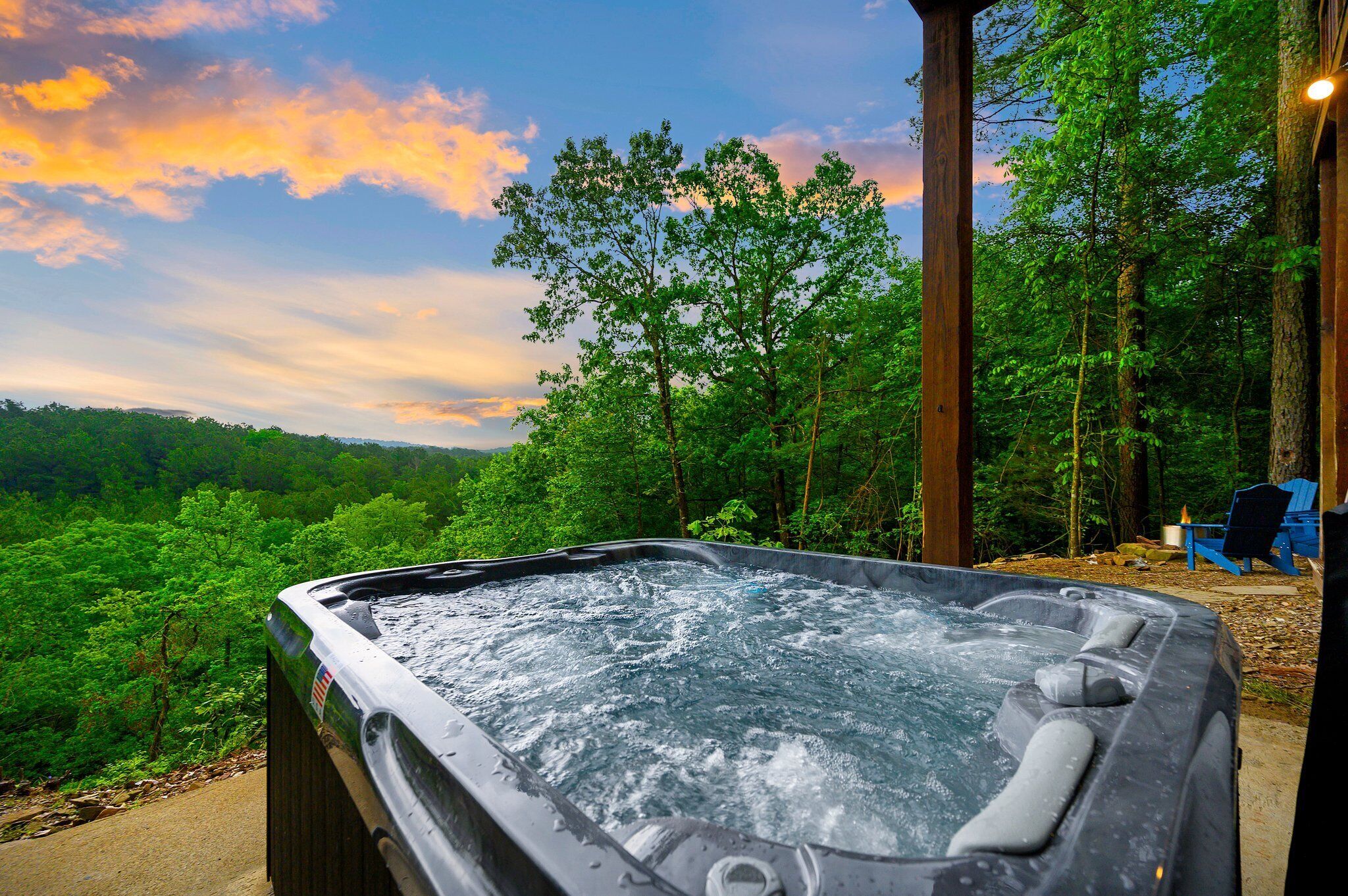 A hot tub in a forested area with a view of trees and a sunset.