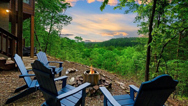 Eine Holzterrasse mit Adirondack-Stühlen und einem Feuerkorb, mit Blick auf eine bewaldete Landschaft.
