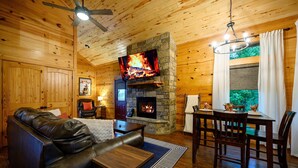 Ein gemütliches Cabin-Interieur mit Kamin aus Stein, Ledersofa, Esstisch und einem Fernseher, der über dem Kamin angebracht ist.