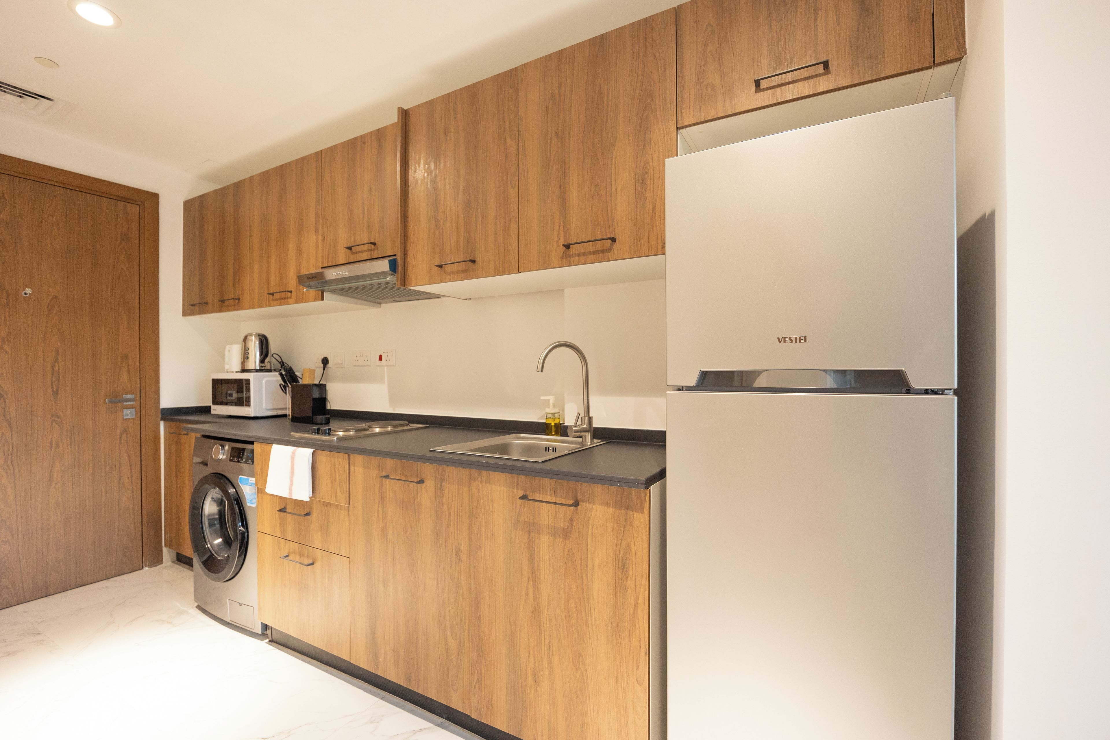 A modern kitchen with wooden cabinets, a built-in washing machine, and a stainless steel refrigerator.
