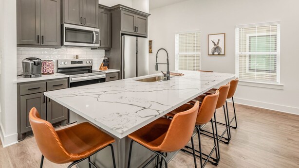 Una cocina moderna con armarios grises, una isla grande con taburetes de bar, microondas, horno y refrigerador.