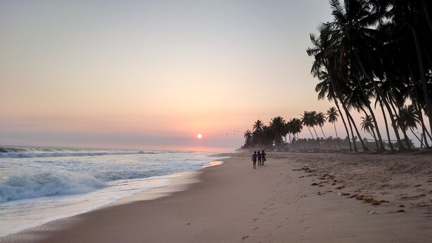 A beach with a sunset, palm trees, and footprints in the sand. - Red Villa on Lionsrest - a tropical garden 500m from the Atlantic beach (Grand Bassam)