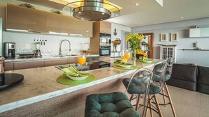 A modern kitchen with a central island, bar stools, and a dining area with a sofa and chairs. - Peninsula Apartment 8-Best View - 3 Bedrooms (Bucerías)