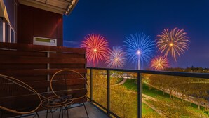 A balcony with two wicker chairs and a view of fireworks.