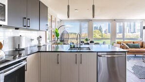 A modern kitchen with a central island, stainless steel appliances, and a view of the city through large windows.