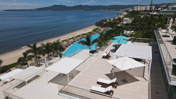A rooftop pool area with lounge chairs and umbrellas, overlooking a beach and ocean. - Penthouse in front of Peninsula Nuevo Vallarta Beach. (Bucerías)