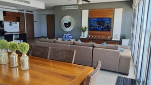 A modern living room with a wooden dining table, grey sofas, and a flat-screen TV mounted on the wall. - Penthouse in front of Peninsula Nuevo Vallarta Beach. (Bucerías)