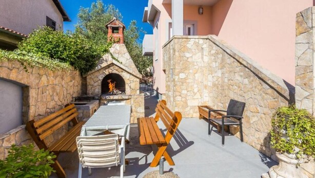 A courtyard with stone walls, wooden benches, a small stone fireplace, and a view of a building with a bell tower. - Modern Apartments in Zadar with Private Terrace - Studio Apartment with Terrace (Zadar)