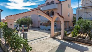 A two-story building with a pink facade, a covered entrance, and a visible balcony. - Modern Apartments in Zadar with Private Terrace - Studio Apartment with Terrace (Zadar)