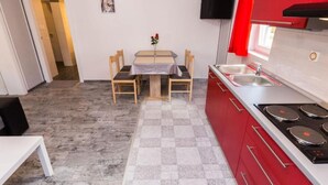 A compact kitchen with a dining table, chairs, a stove, and a TV mounted on the wall. - Modern Apartments in Zadar with Private Terrace - Studio Apartment with Terrace (Zadar)