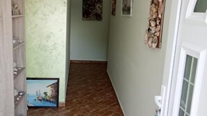 A narrow hallway with a tiled floor, a wooden shelf unit, and a framed picture on the wall.