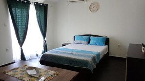 A hotel room with a bed, a desk with a board game, curtains, an air conditioner, and a clock on the wall.