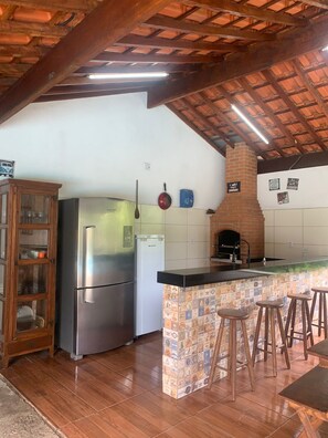 A kitchen with a wooden ceiling, a refrigerator, a dishwasher, and a brick oven.
