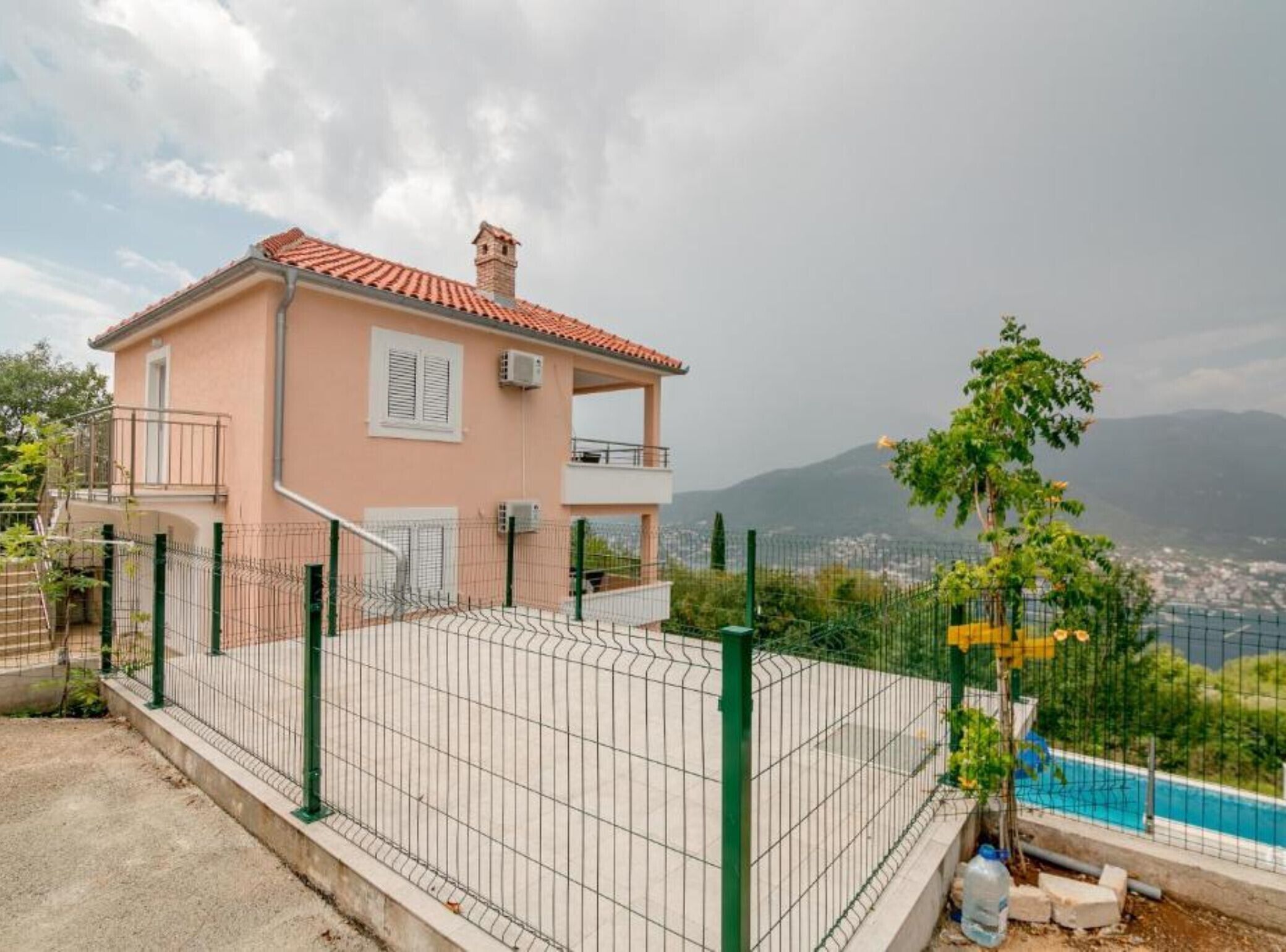Una casa de dos pisos con balcón, un patio cercado y vistas a un paisaje montañoso.